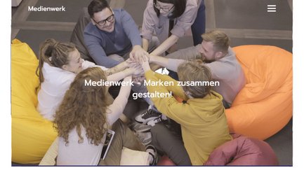 Eine Gruppe von sechs Personen sitzt auf bunten Sitzsäcken und legt ihre Hände in die Mitte, um Teamgeist zu zeigen.