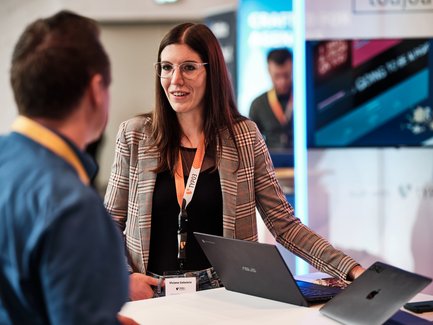 Geschäftliche Gesprächssituation zwischen einer Frau und einem Mann, im Hintergrund ein Screen