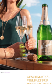 Eine Frau in einem grünen Oberteil hält zwei Gläser Sekt, während eine Flasche Mumm Sekt auf dem Tisch steht.